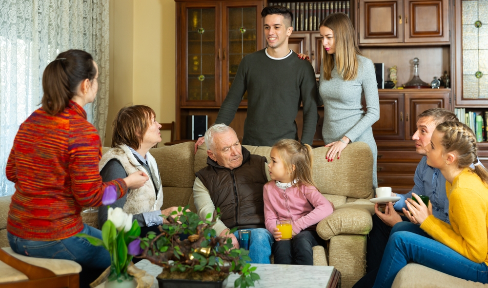 Three generations of a family gathered around an older man in a living room
