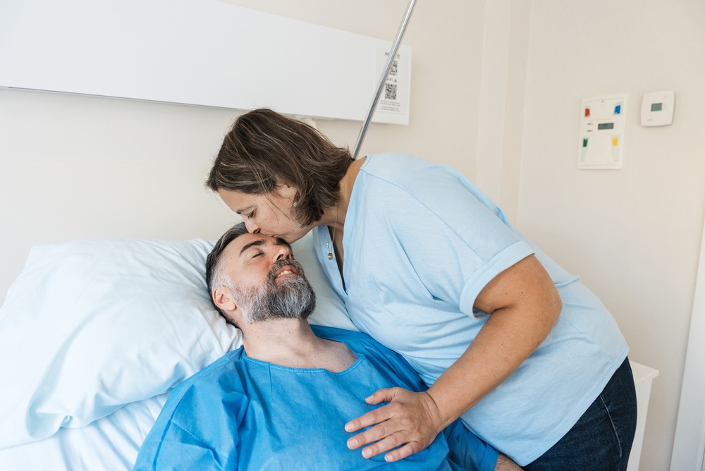 A woman kissing the forehead of a man lying in a hospital bed