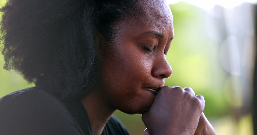 A woman with her eyes closed, pressing her fist to her lips