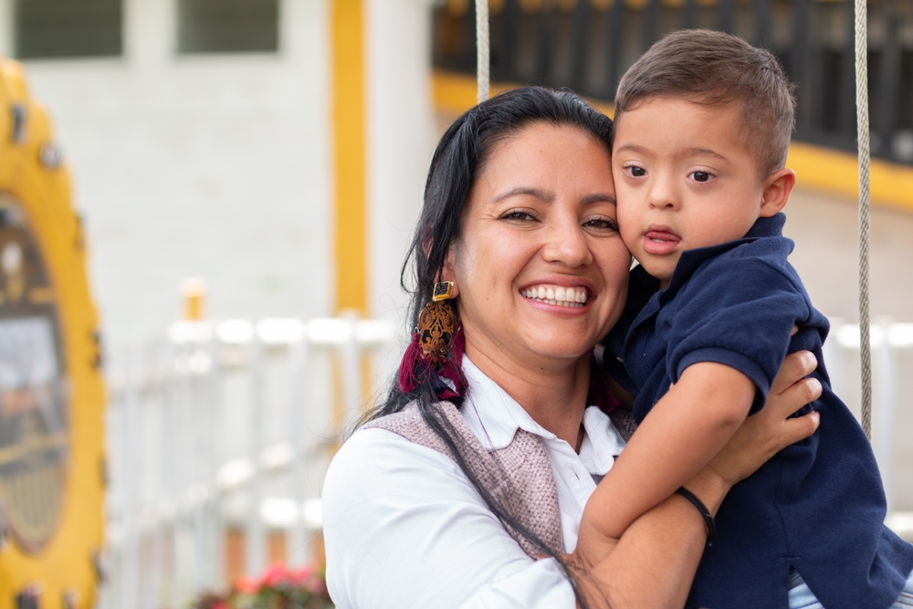 A mother holding her young son close as both smile at a playground