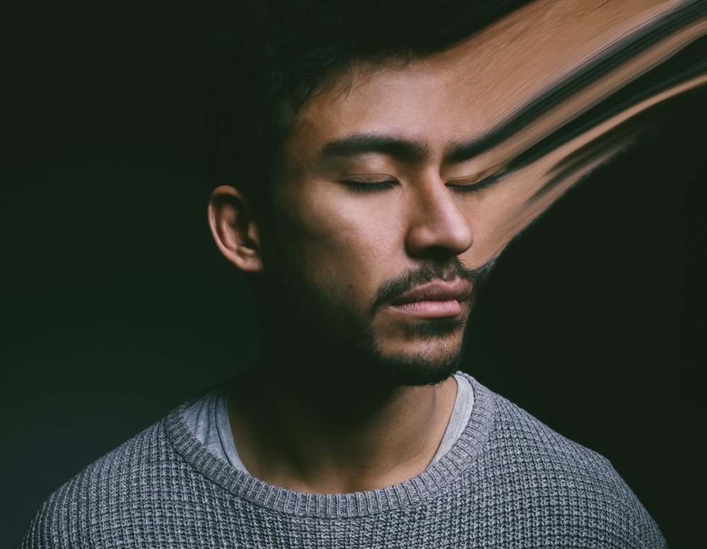 A young man with his eyes closed, lit by a strip of light in a dark room