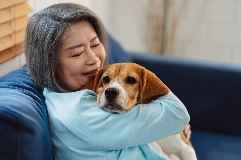 An older woman on a couch hugging a beagle