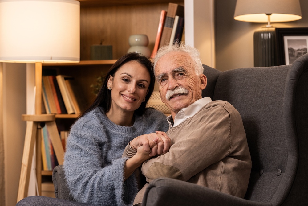 A woman holding hands with her elderly father in his armchair