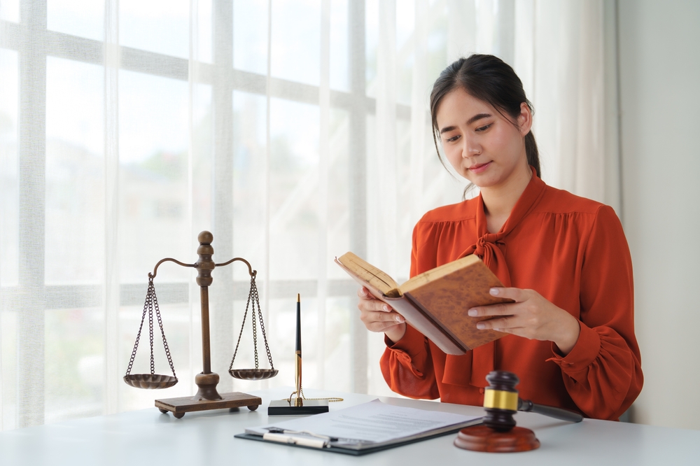 A woman reading a law book at a desk with a scale of justice and a gavel