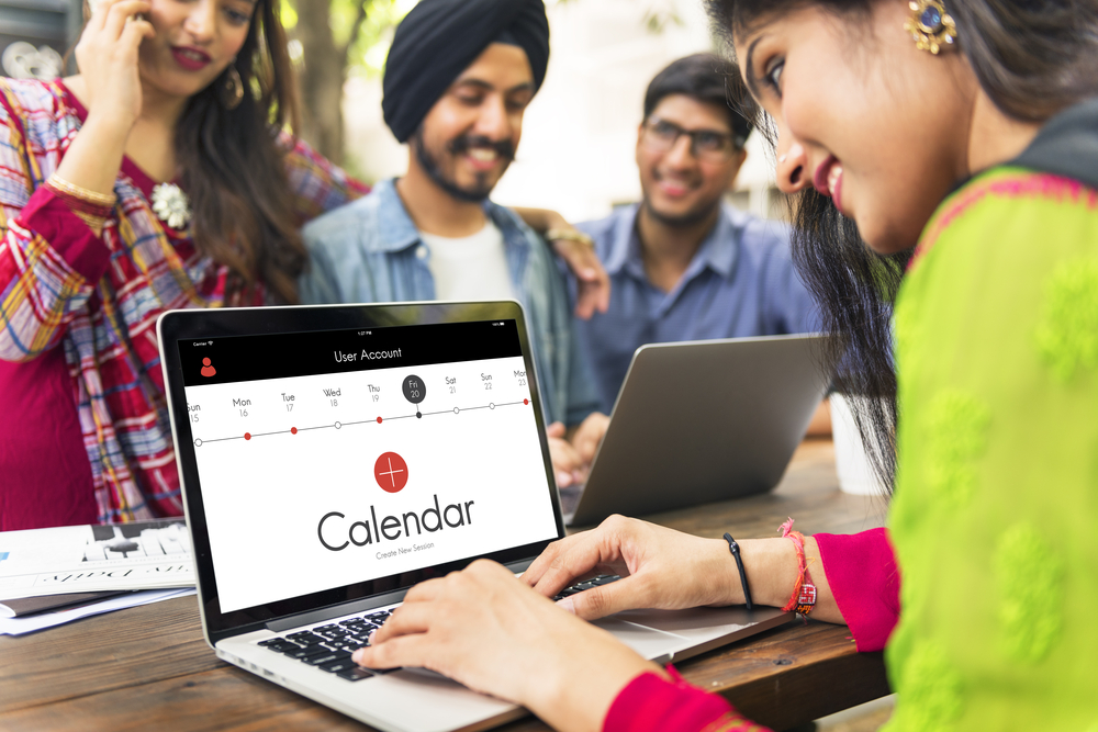 Four friends around a table while one opens a shared calendar on a laptop
