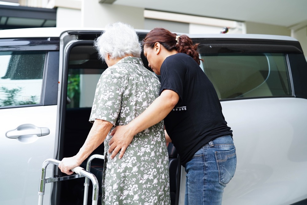 A daughter helping her mother with a walker into the car