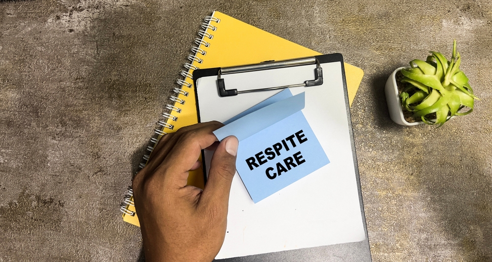 A hand holding a note reading Respite Care over a clipboard and notebook