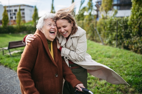 An older woman with a walker laughing with her daughter outdoors