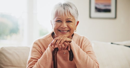 An older woman smiling with her hands resting on her cane