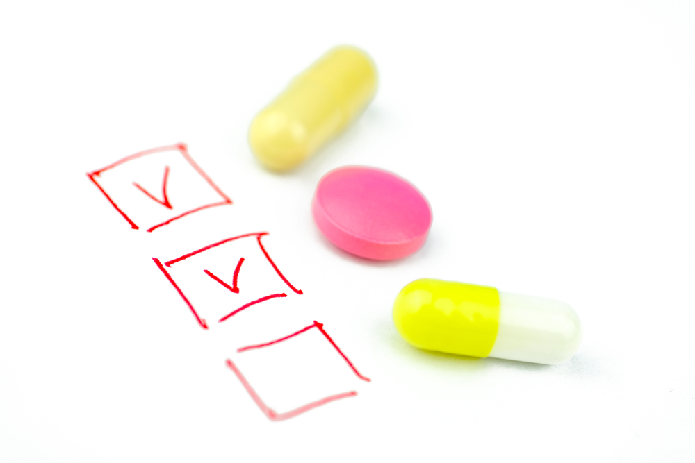 A checklist with two ticked boxes beside three pills on a white table