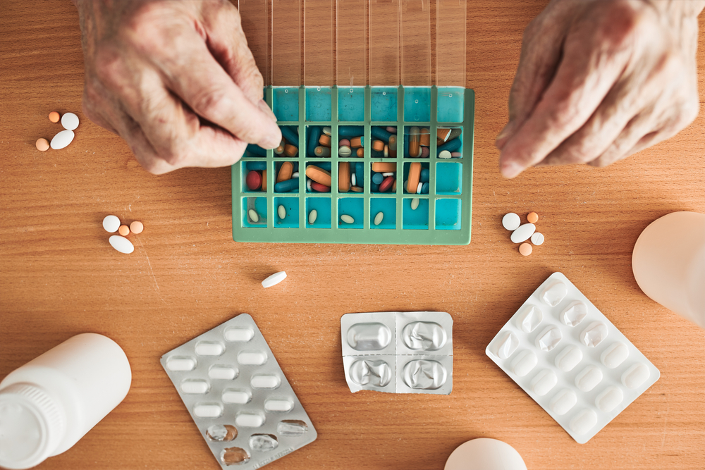 An older person's hands sorting pills into a weekly organizer