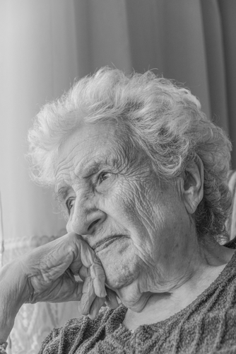 A pensive elderly woman by a window, in black and white