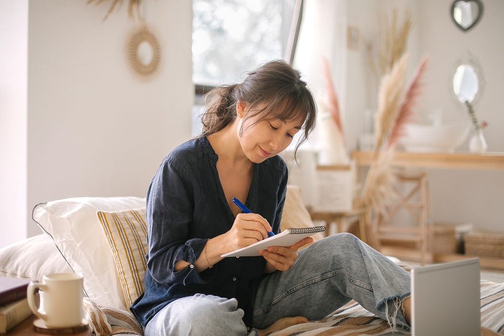 A woman writing a list in a notebook on her bed