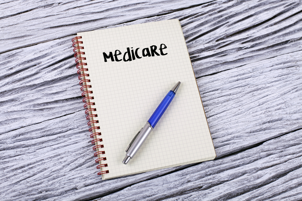 木桌上一本写着 Medicare 的线圈笔记本和一支蓝色钢笔