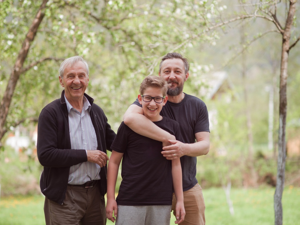 A grandfather, father and son standing together under a tree