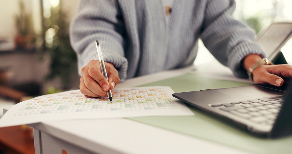 Hands filling in a weekly planner beside a laptop and tablet