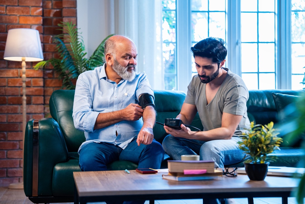An adult son checking his father's blood pressure at home