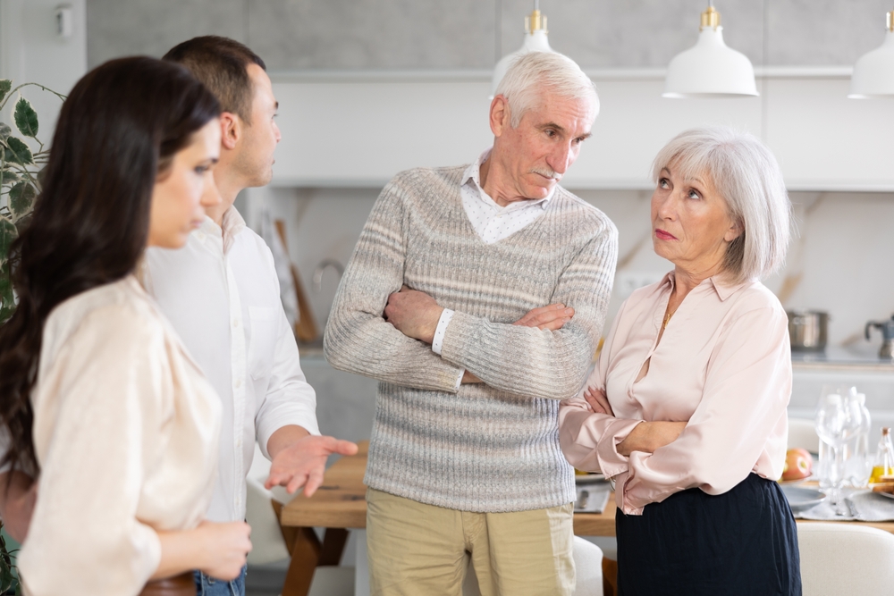 Un couple âgé, bras croisés, face à leurs enfants adultes dans une cuisine