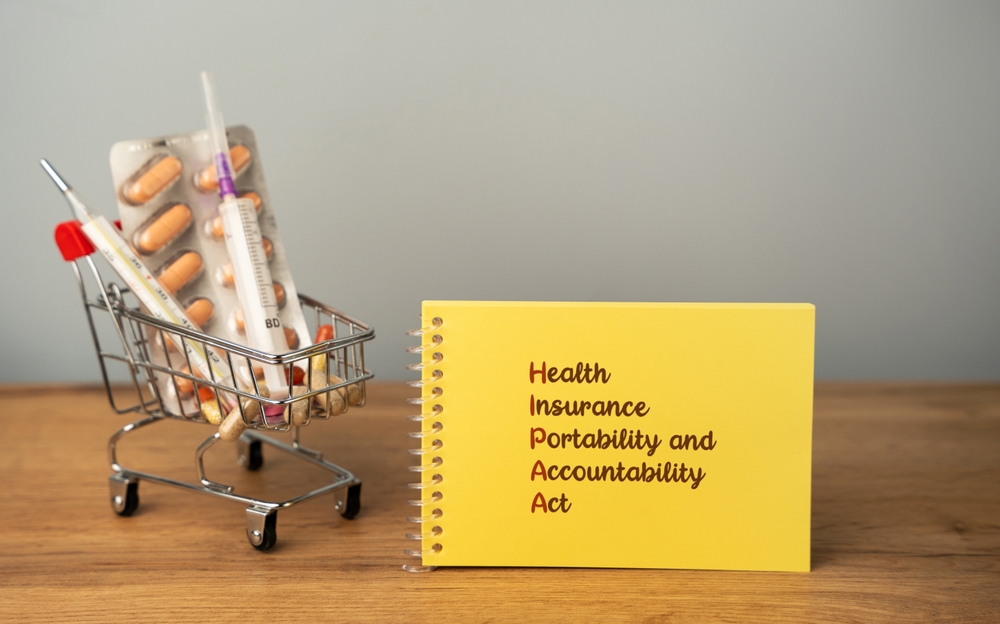 A notepad spelling out Health Insurance Portability and Accountability Act, beside a toy cart of medicines