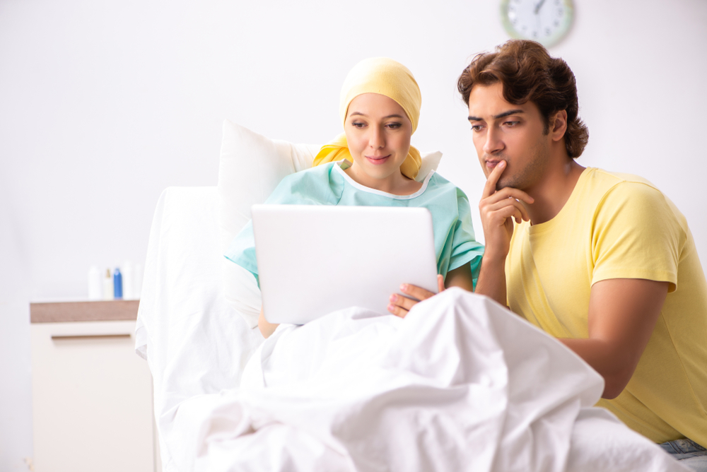A woman in a hospital bed holding a laptop while a man beside her reads it with her