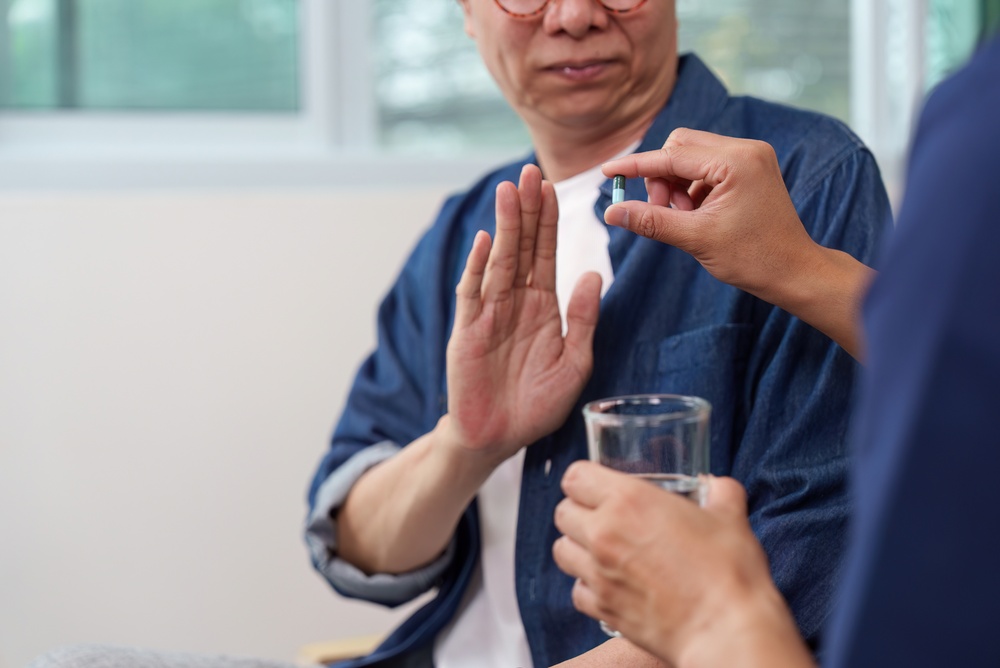 A man holding up his palm to refuse a pill offered by a caregiver
